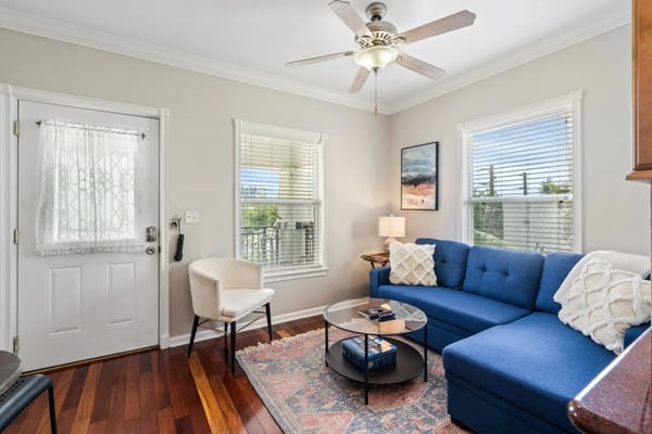 Bright living room with blue sectional sofa, cream armchair, hardwood floors, and multiple windows with views